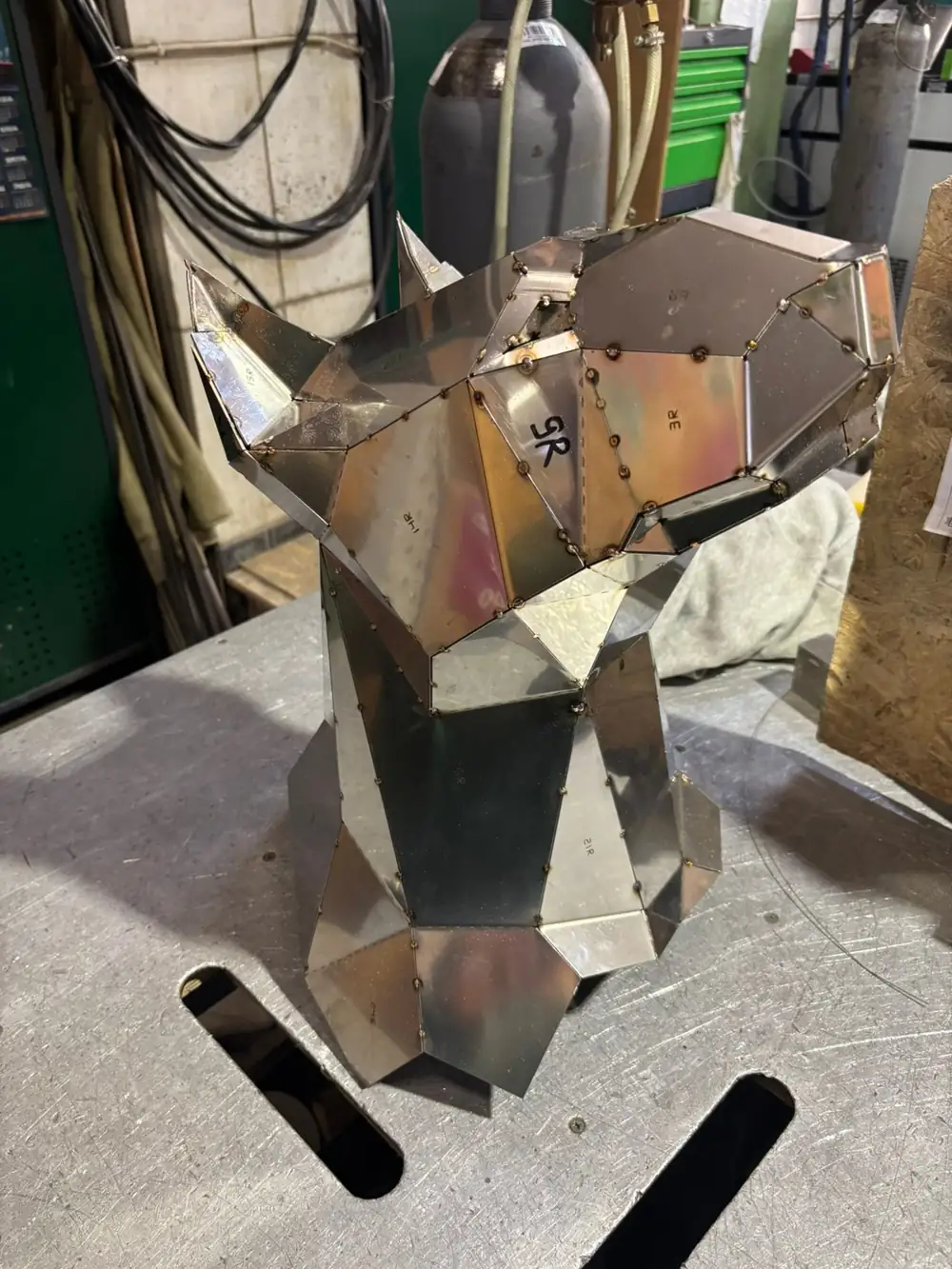 Low-poly steel dog head being tacked together on a welding bench